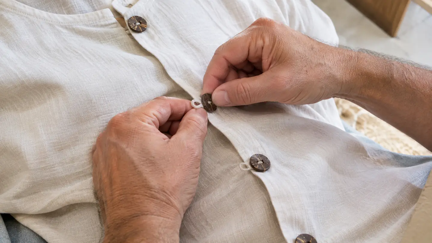 A woman's hands buttoning the coconut-style buttons on a soft Hawaiian shirt