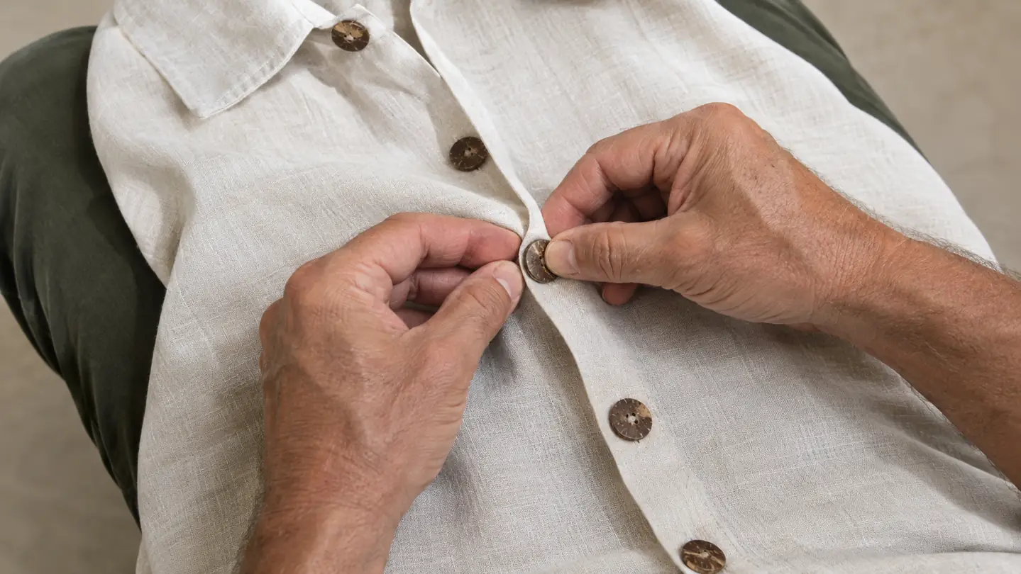 Close view of a woman's hand fastening the coconut-style buttons on a Hawaiian shirt
